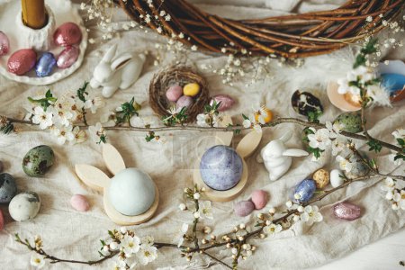 Photo for Happy Easter! Stylish easter eggs, bunnies and cherry blossom  flat lay on rustic table. Modern natural dyed and chocolate colorful eggs and spring flowers. Easter still life  in countryside - Royalty Free Image