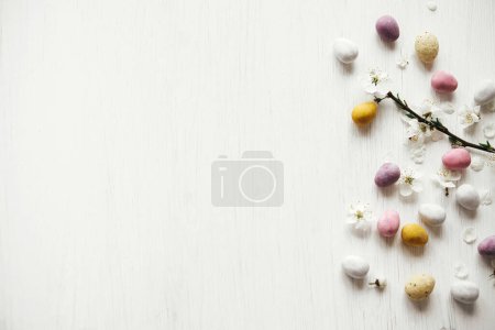 Foto de Pascuas planas. Elegantes huevos de chocolate de Pascua y flor de cerezo en la mesa blanca rústica. ¡Feliz Pascua! Frontera de Pascua con espacio para texto. Dulces modernos huevos coloridos y flores de primavera - Imagen libre de derechos