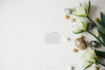 Téléchargez les photos : Des œufs de Pâques et des tulipes élégantes sur une table blanche rustique. Joyeux Pâques ! L'appartement de Pâques. Oeufs en marbre colorant naturel moderne et fleurs de printemps, bannière de vacances. Salutations saisonnières, espace pour le texte - en image libre de droit