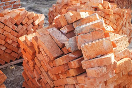 Foto de Stack of red bricks, process of house building. Bricks for laying on concrete foundation. Building materials at construction site - Imagen libre de derechos