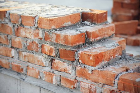 Photo for Bricks masonry with cement on concrete foundation close up, process of house building. Red bricks for laying on concrete foundation. Building materials at construction site - Royalty Free Image