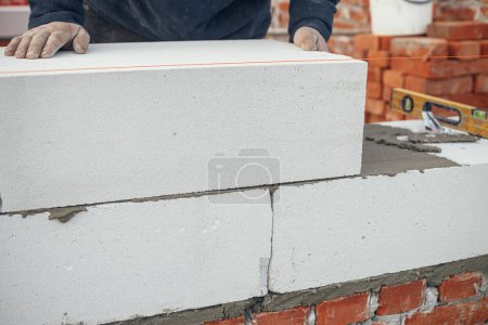 Téléchargez les photos : Constructeur installation de blocs blancs de maçonnerie fermer. Travailleur pose autoclavé blocs de béton aéré. Processus de construction de maisons sur le chantier - en image libre de droit