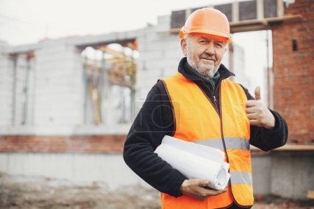 Photo for Senior male foreman in hardhat approving building new modern house according to blueprints. Portrait of happy man engineer or construction worker with plans at construction site - Royalty Free Image