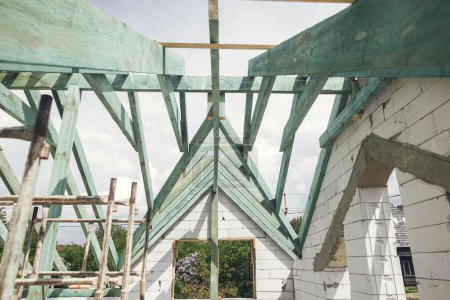 Photo for Unfinished roof trusses, view in attic with rafters, beams, windows and chimney. Wooden roof framing. Mansard of modern farmhouse building construction. - Royalty Free Image