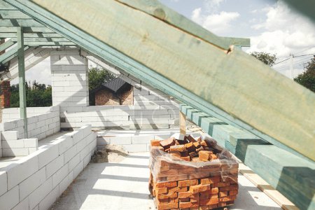 Foto de Wooden roof framing. Unfinished roof trusses and aerated concrete block walls, view in attic with rafters and beams. Modern farmhouse building construction. - Imagen libre de derechos