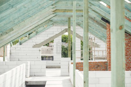 Foto de Wooden roof framing. Unfinished roof trusses and aerated concrete block walls, view in attic with rafters and beams. Modern farmhouse building construction. - Imagen libre de derechos