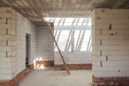 Photo for Unfinished house inside. Aerated concrete blocks wall with windows, doorways and concrete floor in sunny day. Process of house building at construction site. New house construction - Royalty Free Image