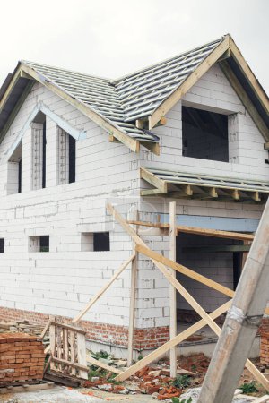 Photo for Unfinished house. Wooden roof framing with vapor barrier and dormer on block walls with windows. New modern farmhouse construction. Timber trusses Rafters and beams on aerated concrete blocks - Royalty Free Image