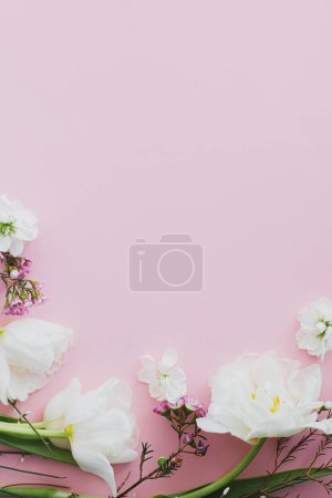 Téléchargez les photos : Joyeuse fête des mères et de la femme. Élégantes fleurs blanches à plat posé sur fond rose, espace pour le texte. Belle tulipes tendres et bordure de fleurs de printemps, modèle de carte de vœux. Bannière florale - en image libre de droit