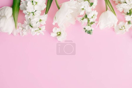 Foto de Feliz Día de las Madres y Día de las Mujeres. Elegantes flores blancas planas yacen sobre fondo rosa, espacio para el texto. Hermosos tulipanes tiernos y borde de flores de primavera, plantilla de tarjeta de felicitación. Banner floral - Imagen libre de derechos