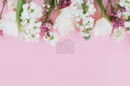 Téléchargez les photos : Joyeuse fête des mères et de la femme. Élégantes fleurs blanches à plat posé sur fond rose, espace pour le texte. Belle tulipes tendres et bordure de fleurs de printemps, modèle de carte de vœux. Bannière florale - en image libre de droit
