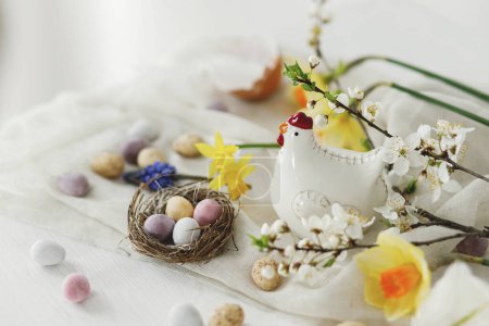 Foto de Naturaleza muerta de Pascua. Huevos de chocolate de Pascua de colores en el nido, flores de primavera, la composición de la figura de pollo en la mesa de madera blanca. Espacio para el texto. ¡Feliz Pascua! Saludos de temporada - Imagen libre de derechos