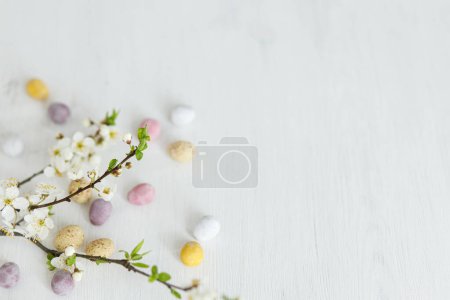 Foto de ¡Feliz Pascua! Elegantes huevos de chocolate de Pascua y suaves flores de primavera en la mesa de madera rústica blanca. Banner simple moderno de Pascua, espacio para el texto. Saludos de temporada - Imagen libre de derechos