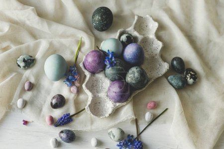 Photo for Happy Easter! Stylish easter eggs in modern tray and spring flowers on linen cloth on rustic white table. Easter simple banner, space for text. Natural painted marble and purple eggs still life - Royalty Free Image