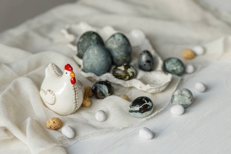 Foto de Elegantes huevos de Pascua en bandeja moderna y figurita de pollo sobre tela de lino sobre mesa blanca rústica. Banner simple de Pascua. ¡Feliz Pascua! Natural pintado huevos de mármol naturaleza muerta - Imagen libre de derechos