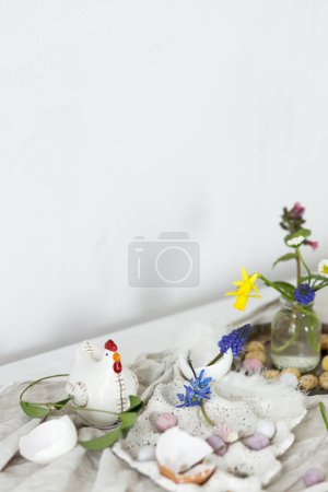 Téléchargez les photos : Joyeux Pâques ! Élégants œufs de Pâques en chocolat, fleurs de printemps, figurines de poulet et tissu de lin sur une table en bois rustique. Espace pour le texte. Pâques décoration simple moderne - en image libre de droit