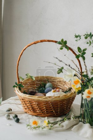 Happy Easter! Stylish easter basket with natural dyed eggs, meat, bread, butter, beets and spring flowers on rustic table. Traditional easter orthodox holiday food and daffodils bouquet