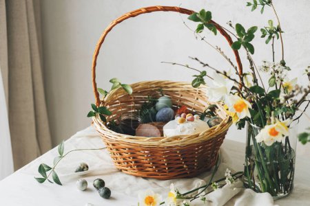 Photo for Stylish Easter basket with eggs and food with spring flowers on rustic table. Happy Easter! Traditional easter holiday food. Modern natural dye eggs, tasty ham, bread, butter, beets - Royalty Free Image