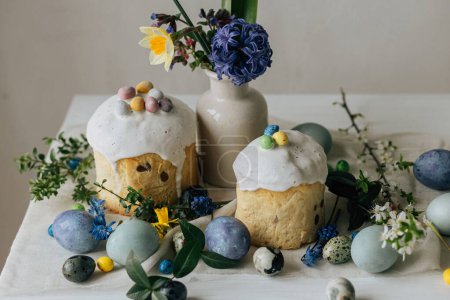 ¡Feliz Pascua! Elegantes huevos de Pascua, pan casero de Pascua y flores de primavera en la servilleta de lino en la mesa rústica. Huevos de mármol pintados naturales, flores y comida navideña. Bodegón moderno