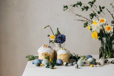 ¡Feliz Pascua! Elegantes huevos de Pascua, pan casero de Pascua y flores de primavera en la servilleta de lino en la mesa rústica. Huevos de mármol pintados naturales, ramillete de narcisos y comida navideña. Bodegón moderno