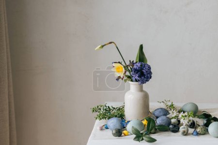 Foto de ¡Feliz Pascua! Elegantes huevos de Pascua y flores de primavera en servilleta de lino en la mesa rústica. Mármol pintado natural y huevos azules, flores de jacinto y narcisos. Moderno bodegón mínimo - Imagen libre de derechos