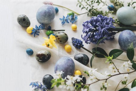 Foto de ¡Feliz Pascua! Elegantes huevos de Pascua y flores de primavera en servilleta de lino en la mesa rústica. Mármol pintado natural y huevos azules, flores de jacinto y narcisos. Moderno bodegón mínimo - Imagen libre de derechos