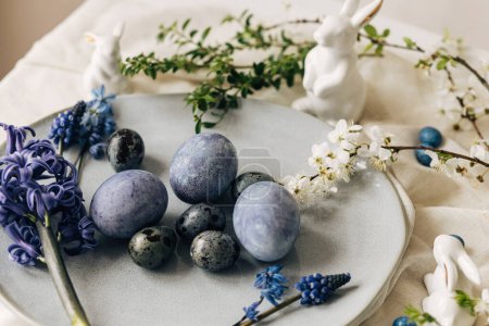 Photo for Stylish easter eggs on vintage plate, bunny and spring flowers on rustic table. Happy Easter! Natural dye blue eggs, purple hiacynt blossoms on linen napkin. Holiday setting, minimal still life - Royalty Free Image