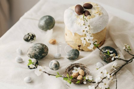 Photo for Stylish easter eggs, panettone, spring flowers and chocolate eggs on linen cloth on rustic table. Natural dye marble eggs and cherry blossom, minimal still life. Happy Easter! - Royalty Free Image