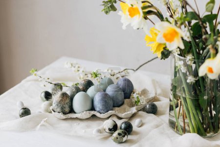 Photo for Stylish Easter eggs and spring flowers on rustic table. Happy Easter! Natural dye marble and blue eggs in tray and daffodils bouquet. Happy Easter! Holiday minimal still life - Royalty Free Image