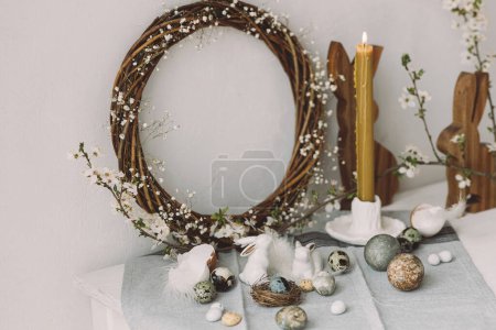 Photo for Stylish easter eggs, wooden bunnies, cherry blossom and candle composition on rustic table. Happy Easter! Modern natural dyed marble eggs and spring flowers. Rural still life - Royalty Free Image