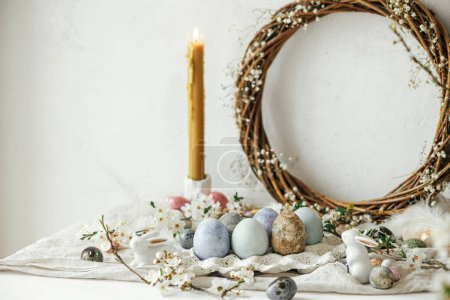 Foto de Elegantes huevos de Pascua, conejos y composición de flores de cerezo en mesa rústica. ¡Feliz Pascua! Modernos huevos naturales teñidos y de chocolate y flores de primavera. Naturaleza muerta rural - Imagen libre de derechos
