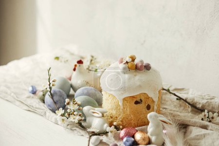 Foto de ¡Feliz Pascua! Elegantes huevos de Pascua, pastel, conejos, flor de cerezo en la mesa rústica. Huevos teñidos naturales modernos, comida navideña y flores de primavera. Campo de Pascua naturaleza muerta - Imagen libre de derechos