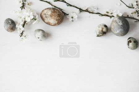 Téléchargez les photos : Joyeux Pâques ! Des œufs de Pâques élégants et des fleurs de cerisier sur une table blanche rustique reposent à plat. Oeufs en marbre colorant naturel moderne et fleurs de printemps. Modèle de bordure de Pâques minimal avec espace pour le texte - en image libre de droit