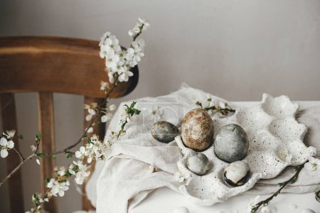 Foto de ¡Feliz Pascua! Elegantes huevos de Pascua en bandeja y flor de cerezo en mesa rústica. Modernos huevos de mármol de tinte natural y flores de primavera bodegón. Composición rural de Pascua - Imagen libre de derechos