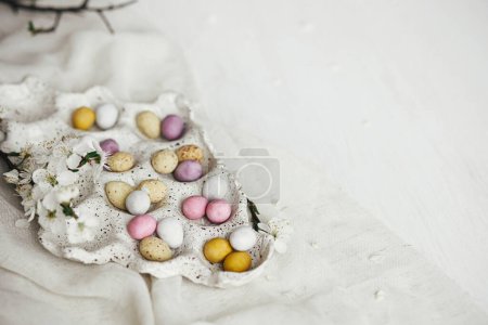 Foto de ¡Feliz Pascua! Elegantes huevos de Pascua de colores en bandeja y flor de cerezo en la mesa rústica plana ponen. Huevos naturales de chocolate con flores de primavera. Espacio para texto - Imagen libre de derechos