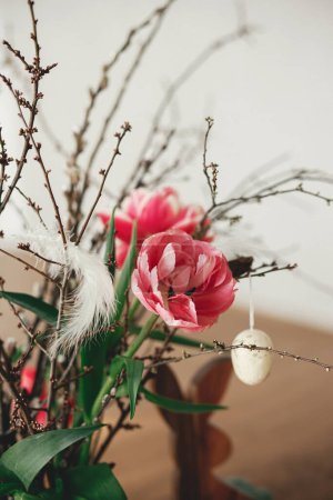 Téléchargez les photos : Bouquet élégant de tulipes avec branches de saule, oeufs de Pâques et décor de plumes sur table en bois fermer. Joyeux Pâques ! Décor de table de Pâques simple dans le salon de la ferme - en image libre de droit