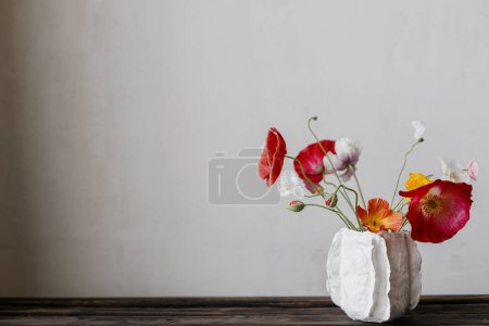 Flowers in modern vase rustic still life. Beautiful red and yellow poppies on aged wooden bench. Summer wildflowers, floral wallpaper. Space for text