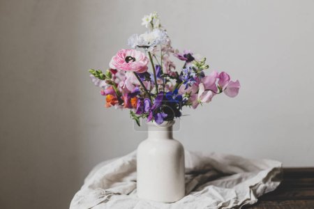 Summer flowers in vase, rustic moody still life. Beautiful colorful anemone, ranunculus, lathyrus, scabiosa on aged bench with linen cloth. Floral moody wallpaper. Space for text