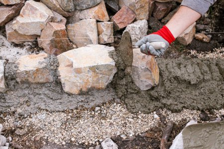 Téléchargez les photos : Travailleur installant des pierres pour le chemin dans le jardin de chalet. Gros plan de la maçonnerie de roche et de béton, constructeur faisant bord pour le chemin dans le jardin urbain moderne - en image libre de droit