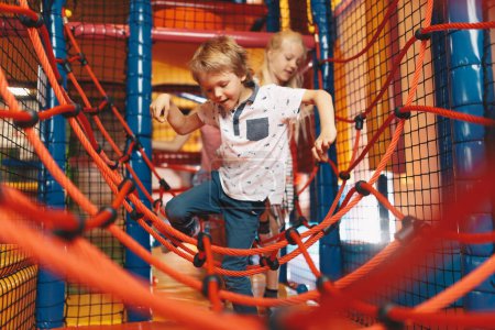 Photo for Excited kids playing together on net ropes. Happy group of siblings playing together on indoor playground. Cute school kids playing on the colorful playground at shopping mall - Royalty Free Image