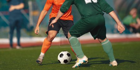 Foto de Two adult football players kicking soccer ball in a duel. Soccer competition between two teams. Anonymous players running and kicking ball - Imagen libre de derechos