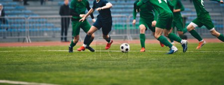 Fußballer führen ein Spiel aus und kicken Fußball. Europäisches Fußballspiel zwischen Spielern in grünen und blauen Uniformen. Bundesligaspiel