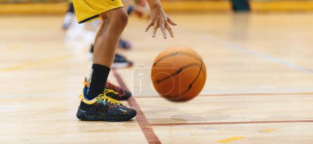 Horizontal image of young basketball player bouncing ball in training drill. Youth basketball team on training. Basketball training session for school kids. Junior-level basketball player in a game