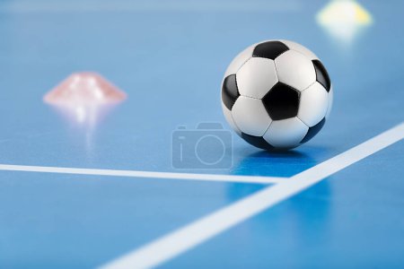 Futsal practice pitch. Indoor soccer ball and training equipment on blue futsal floor. Football pitch sidelines and training cones