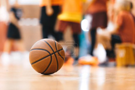 Photo for Basketball Ball On Hardwood Floor Youth Basketball Team in Background. Indoor Sports Training Unit for School Kids - Royalty Free Image