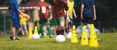 Photo for Slalom practice for football players. Youth in sports training. Player kicking ball during a soccer training drill. Summer sports practice camp for school kids - Royalty Free Image