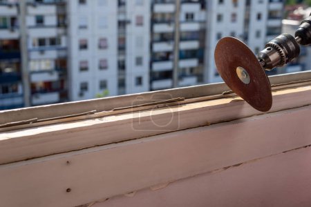 Foto de Sanding an old window frame during renovation work with an apartment building in a background - Imagen libre de derechos