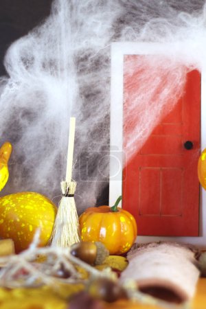 Photo for Vertical image of a red door, surrounded by cobwebs and at the entrance of the door pumpkins and a witch's broom. Does she live there? - Royalty Free Image