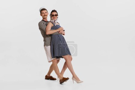 Portrait of young sailor in striped shirt dancing with beautiful young woman isolated over white background. Concept of summer holidays, occupation, retro fashion, vintage style. Copy space for ad