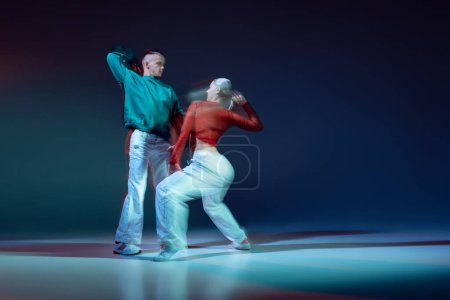 Foto de Retrato de jóvenes, hombres y mujeres bailando hip-hop aislados sobre fondo azul oscuro con luces mixtas. Concepto de movimiento, cultura juvenil, estilo de vida activo, acción, danza callejera, hobby, anuncio - Imagen libre de derechos